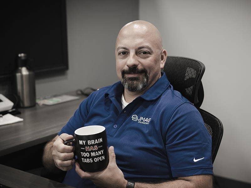 JMag employee sitting in chair at work and showing his coffee mug